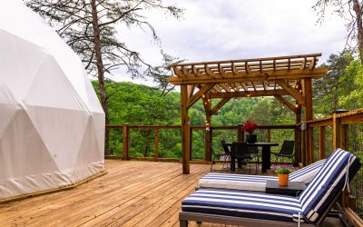 Exterior view of a glamping dome on a deck with striped lounge chairs and a wooden pergola
